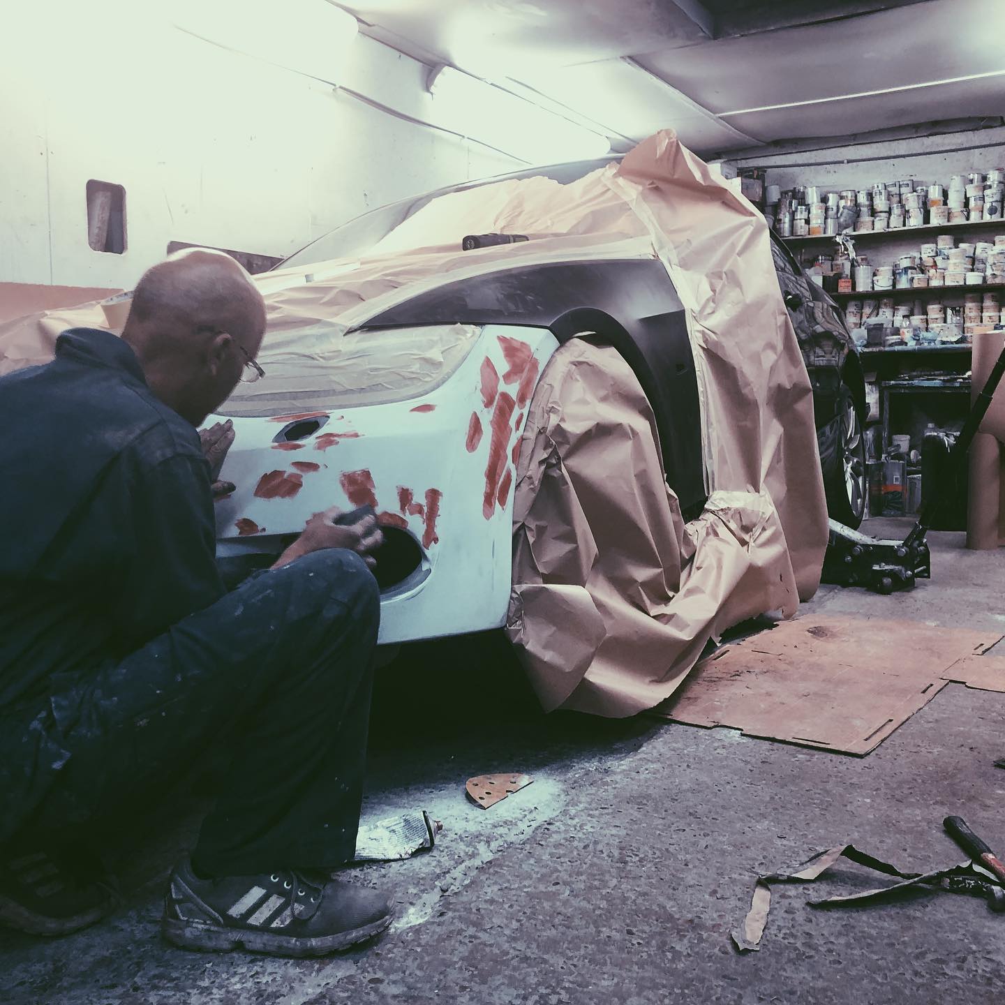 Technician preparing primer filler on a sports car panel before respray